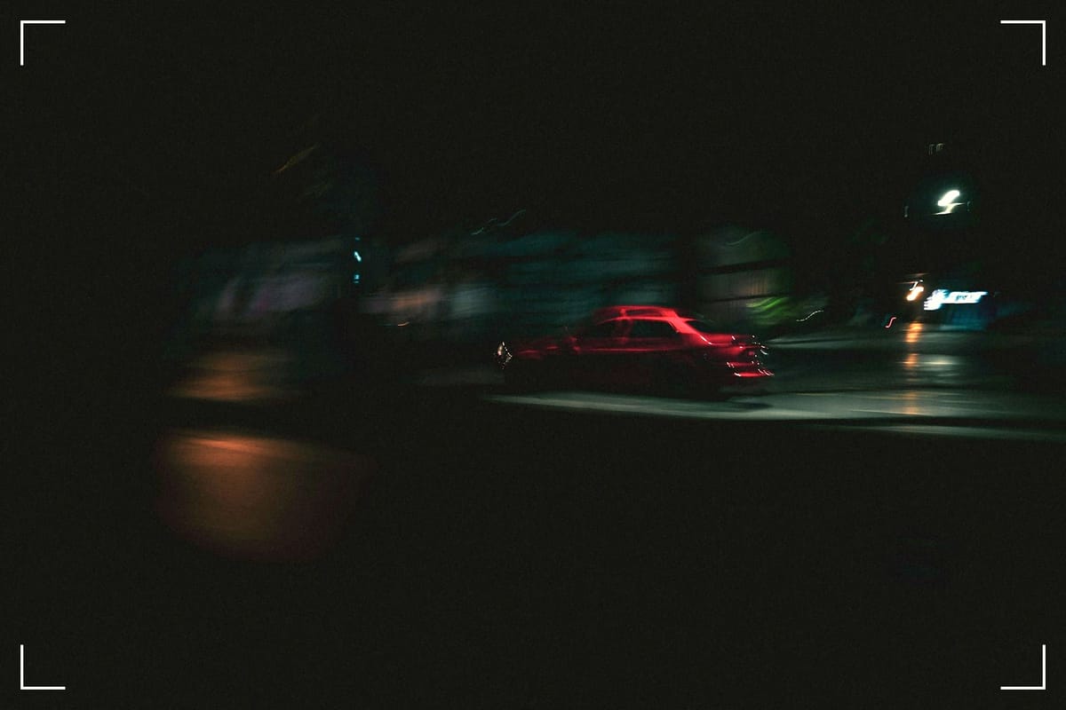A blurry picture of a red cab (taxi) at night in something that looks like an empty street.