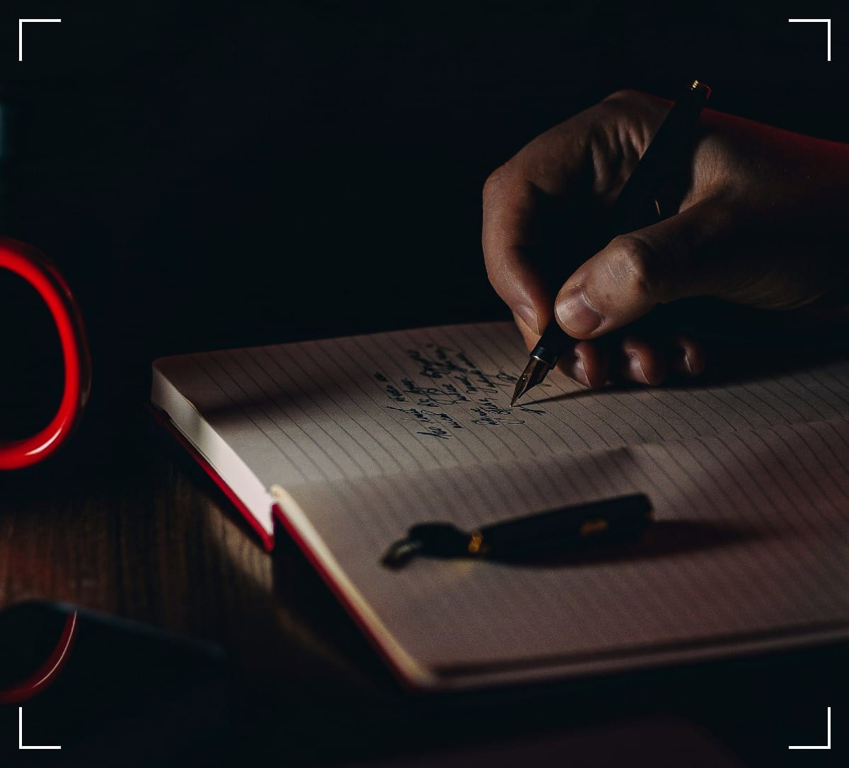 A hand with a fountain-pen writing in a lined notebook.