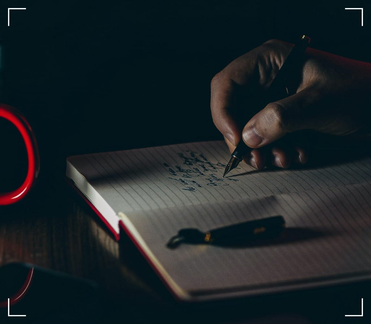 Close-up photograph of a hand holding a fountain-pen and writing something in a lined notebook.