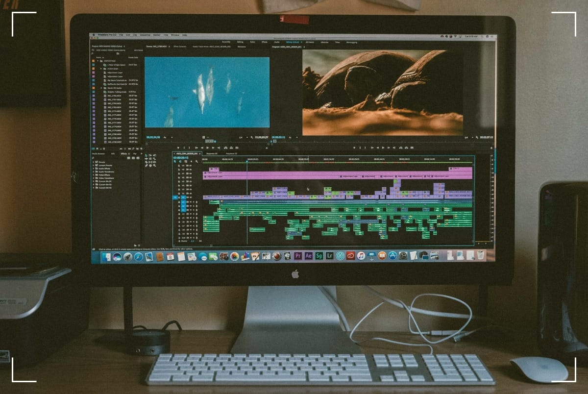 An Apple screen showing a video editing software. There is a white Apple keyboard in front of the screen and an Apple mouse to the right of the keyboard.