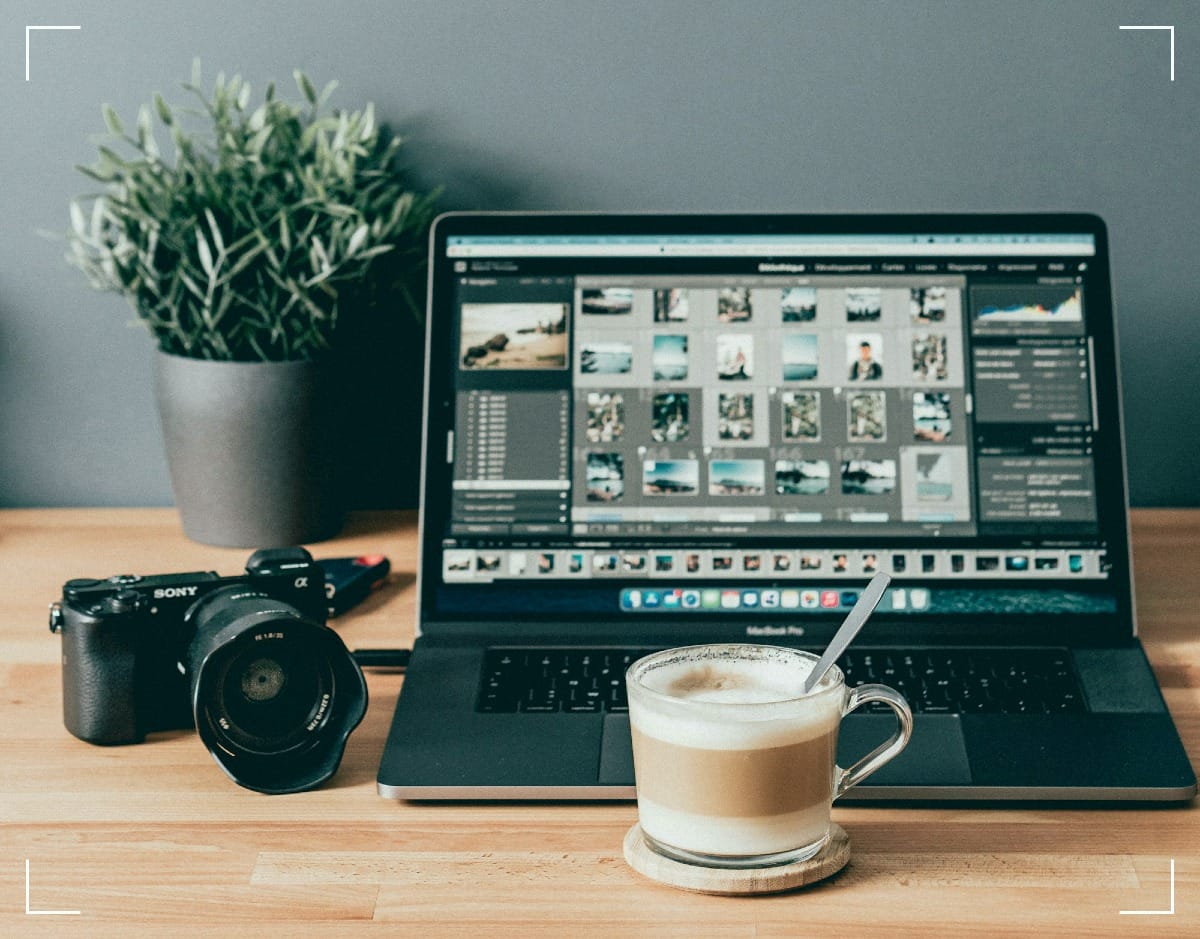 A macbook laptop with Lightroom running. There is a camera to the left of the image and a cup of coffee in front.