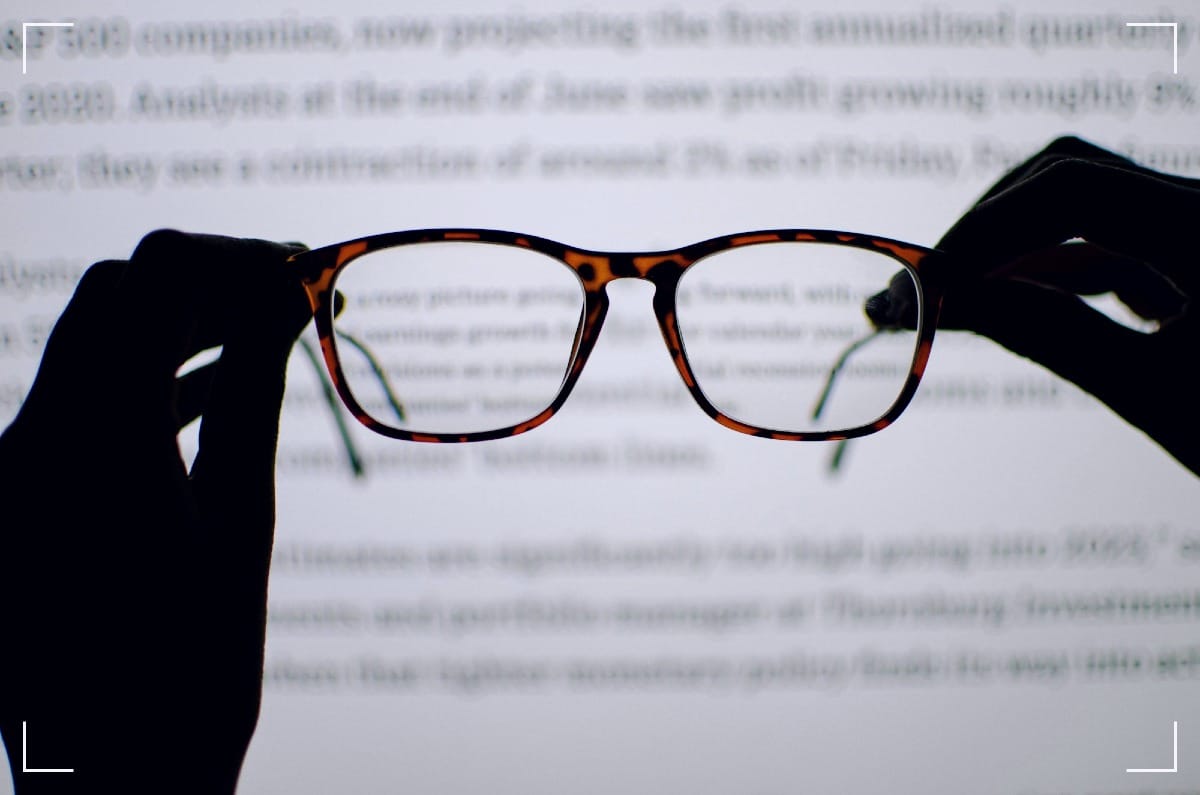 A pair of glasses in front something that looks like a screen withan Internet site. De glasses are sharp and in front while the webpage is behind the glasses and out of focus.